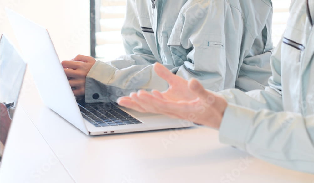 作業着を着た人物たちがノートパソコンを使いながら打ち合わせをしている様子