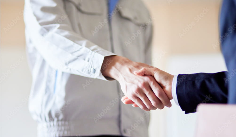 作業服を着た人物とスーツ姿の人物が握手を交わしているシーン