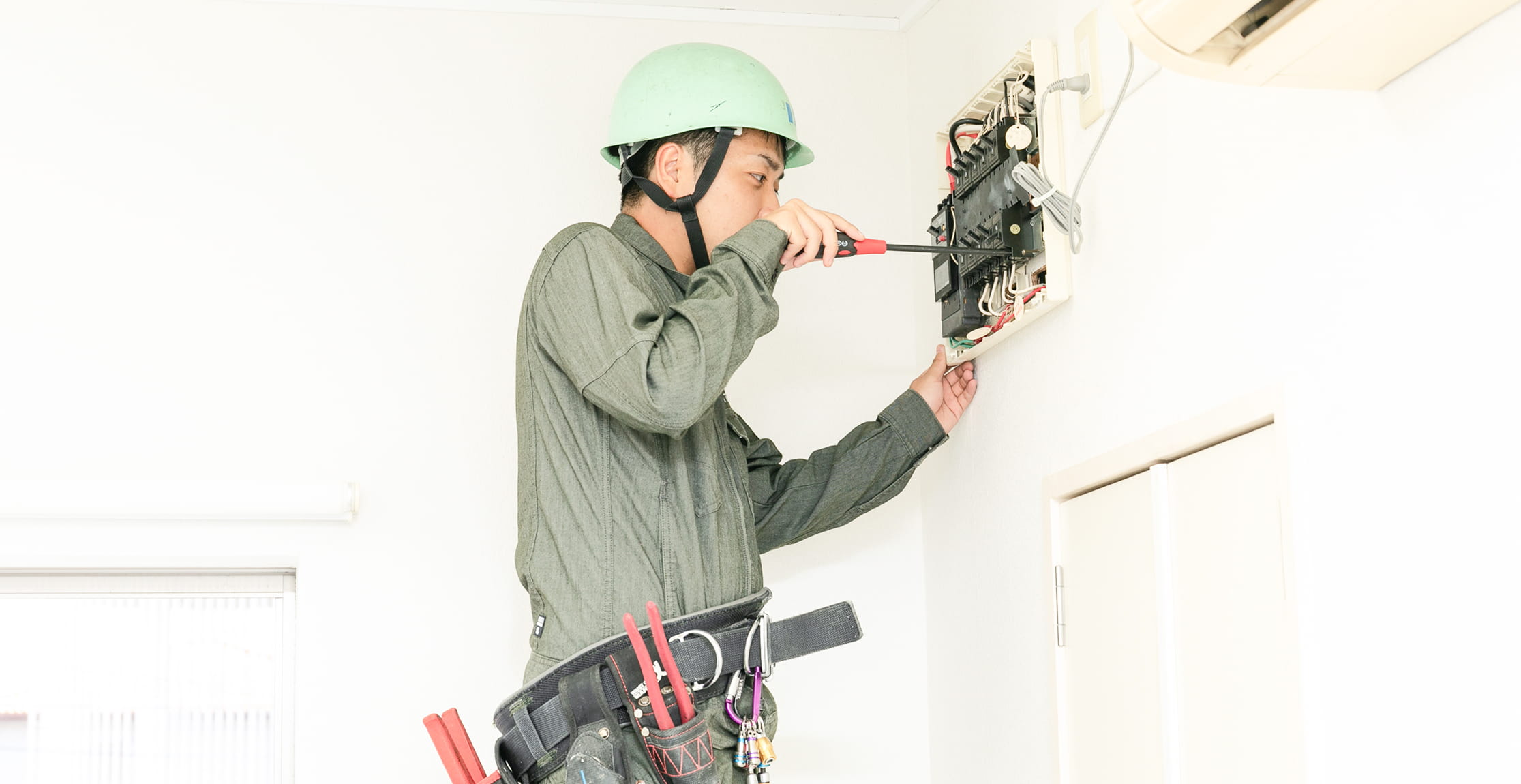 作業服とヘルメットを着用した男性が、配電盤の内部を点検・整備している