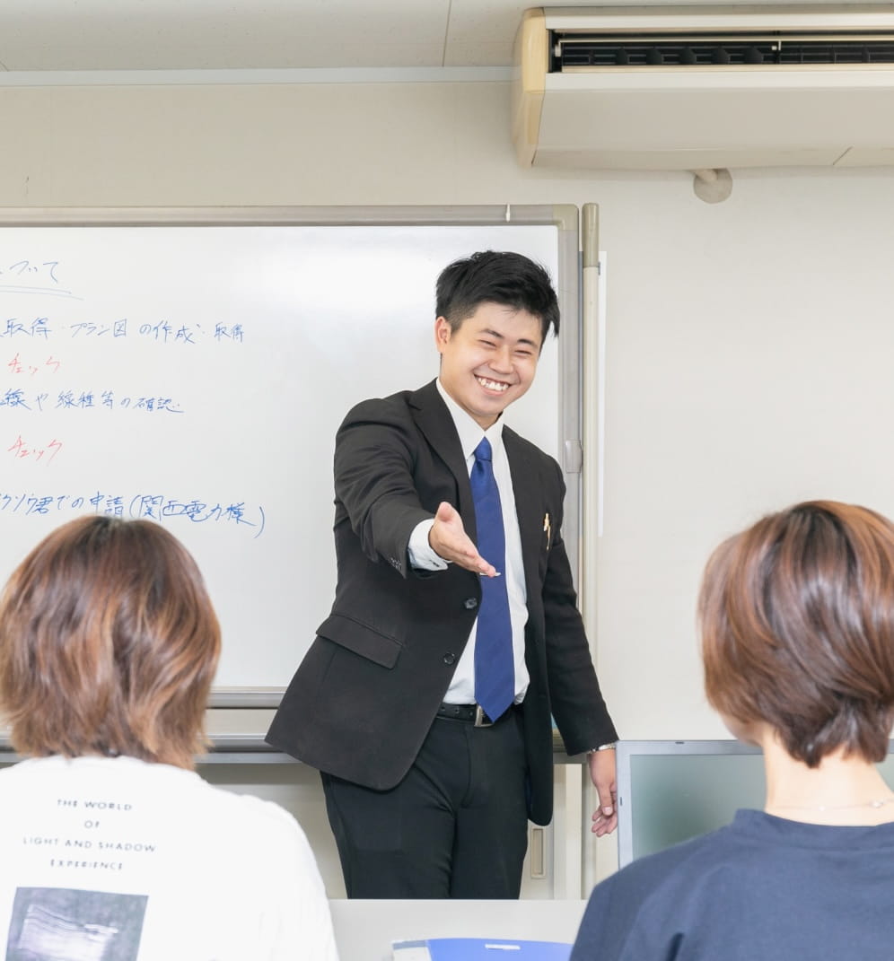 スーツ姿の男性がホワイトボード前で笑顔を見せながら受講者に語りかけている