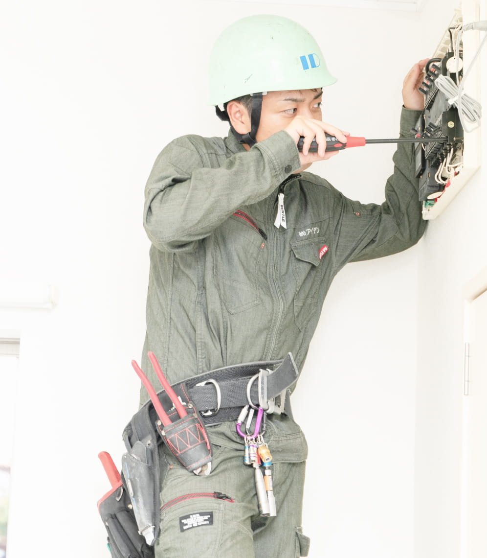 作業服とヘルメットを着用した男性が、配電盤の配線作業を行っている